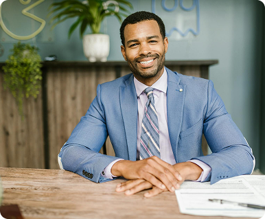 A professional man in a suit smiling at a desk.